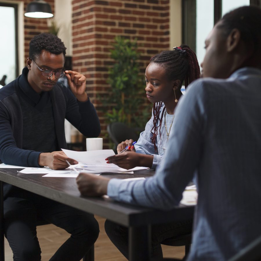 African american research agency coworkers in meeting about startup project financial status. Business people at desk in company office finance department talking about marketing expenses.